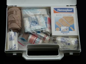 Open white first aid case stocked with rolled bandages, gauze, and adhesive dressings