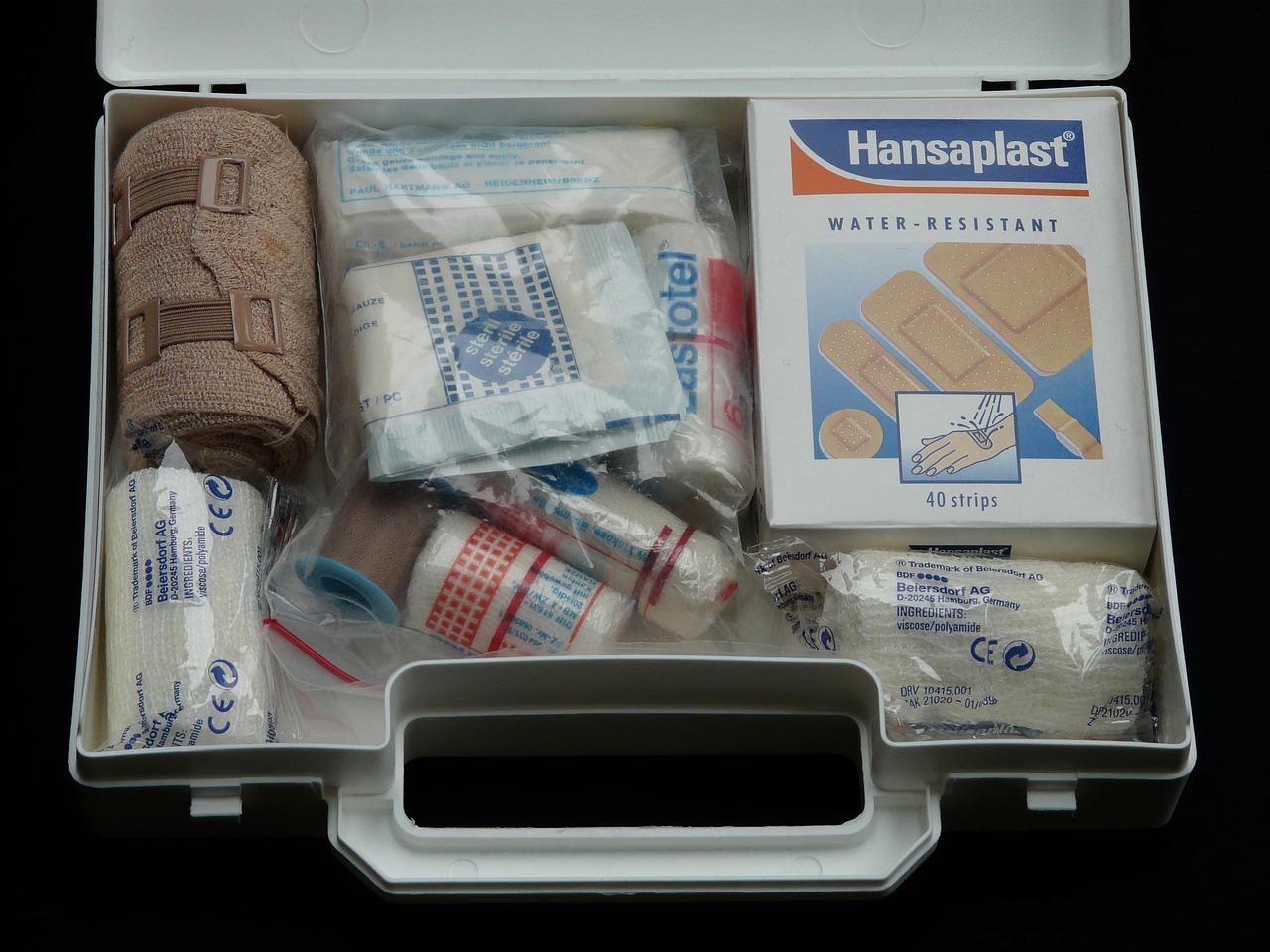 Open white first aid case stocked with rolled bandages, gauze, and adhesive dressings